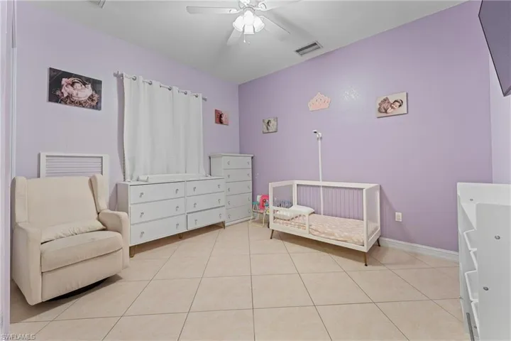 Tiled bedroom featuring ceiling fan and a crib