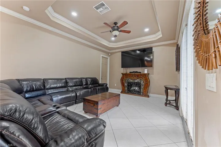 Tiled living room with ceiling fan, a tray ceiling, crown molding, and a premium fireplace