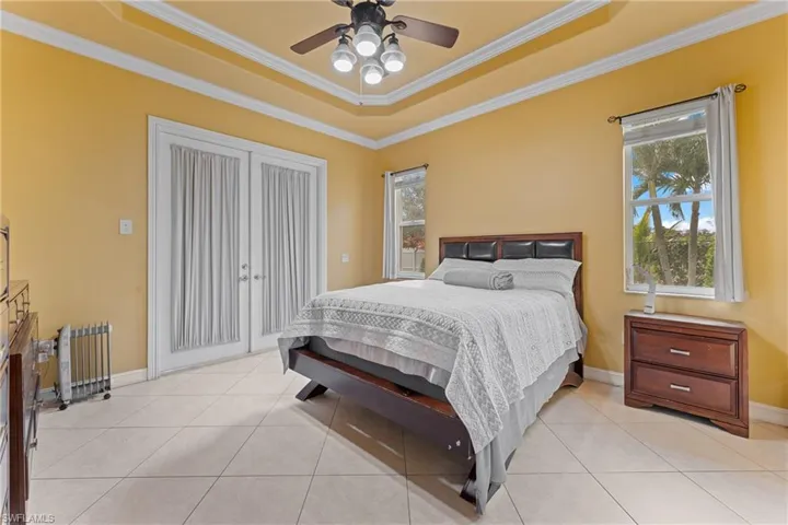 Bedroom featuring ceiling fan, light tile patterned flooring, ornamental molding, and a raised ceiling