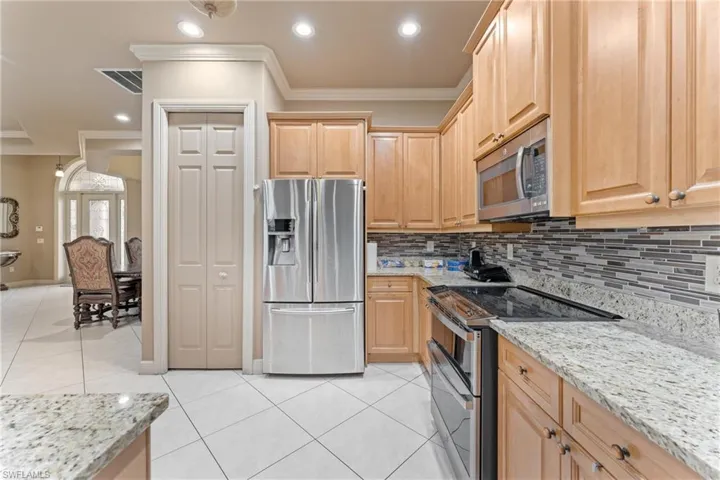 Kitchen with stainless steel appliances, ornamental molding, light brown cabinets, and light stone countertops