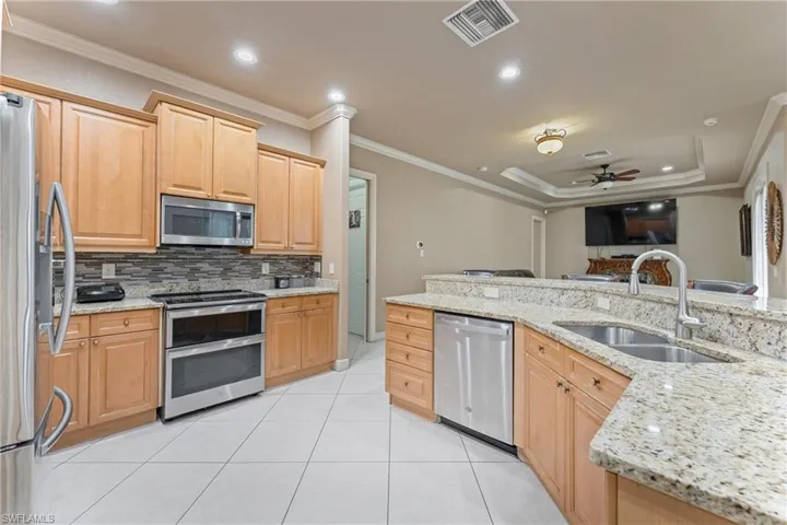 Kitchen with ceiling fan, appliances with stainless steel finishes, light stone countertops, crown molding, and sink