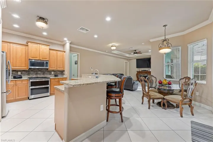 Kitchen with stainless steel appliances, an island with sink, ornamental molding, ceiling fan, and light stone counters