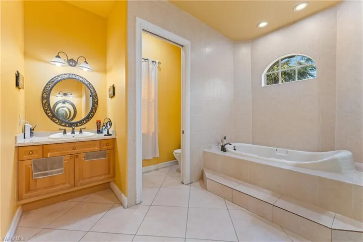 Bathroom with tiled tub, toilet, vanity, and tile patterned flooring