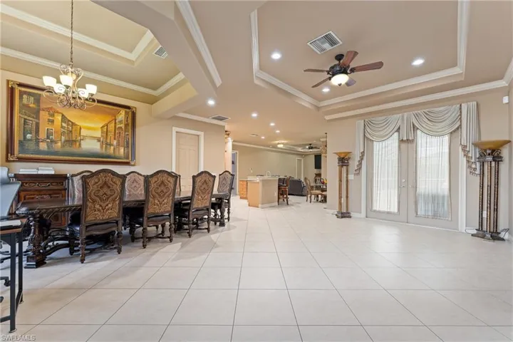 Dining space featuring ceiling fan with notable chandelier, light tile patterned floors, a tray ceiling, and crown molding