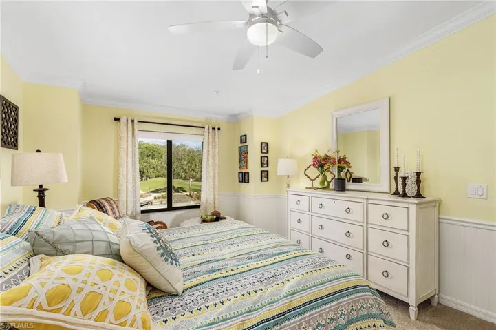Bedroom with a wainscoted wall, crown molding, ceiling fan, and light carpet