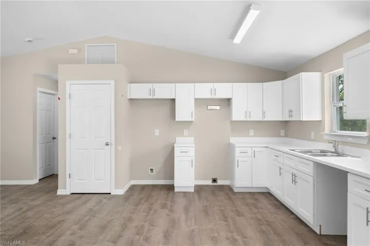 Kitchen with sink, vaulted ceiling, light hardwood / wood-style floors, and white cabinetry