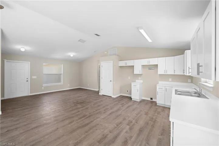 Kitchen featuring sink, hardwood / wood-style floors, lofted ceiling, and white cabinetry