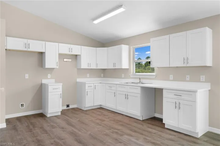 Kitchen featuring sink, white cabinets, lofted ceiling, and hardwood / wood-style flooring