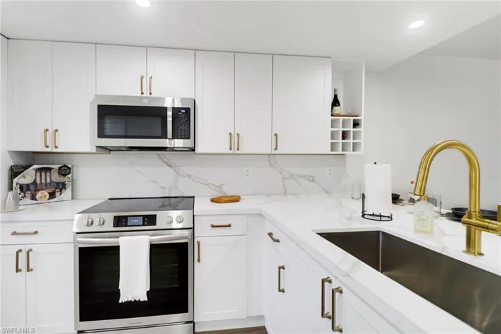 Kitchen featuring light stone counters, appliances with stainless steel finishes, a sink, white cabinetry, and backsplash