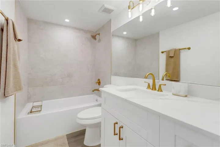 Full bathroom with toilet, recessed lighting, vanity, visible vents, and washtub / shower combination
