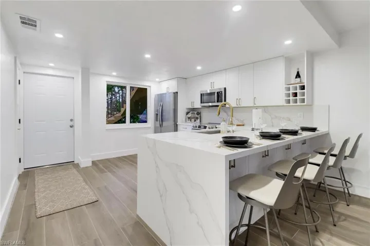Kitchen featuring appliances with stainless steel finishes, a peninsula, light stone countertops, white cabinetry, and open shelves