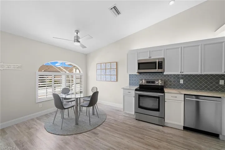 Kitchen with stainless steel appliances, vaulted ceiling, white cabinetry, and ceiling fan