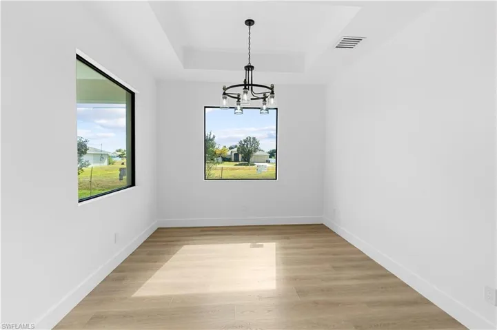 Unfurnished dining area with a chandelier, light wood-style floors, and a raised ceiling