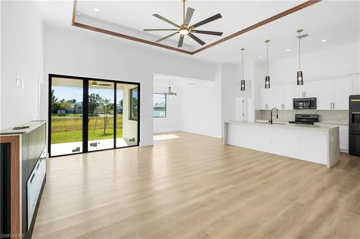 Unfurnished living room with a towering ceiling, light wood finished floors, a chandelier, ceiling fan, and recessed lighting