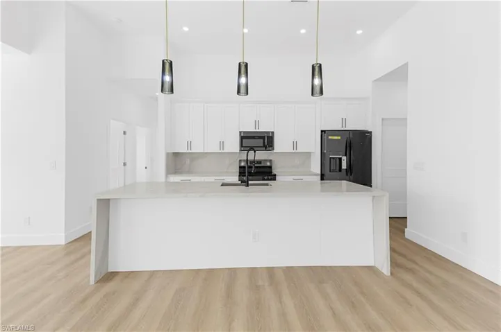 Kitchen featuring light stone countertops, a high ceiling, white cabinetry, black fridge, and pendant lighting