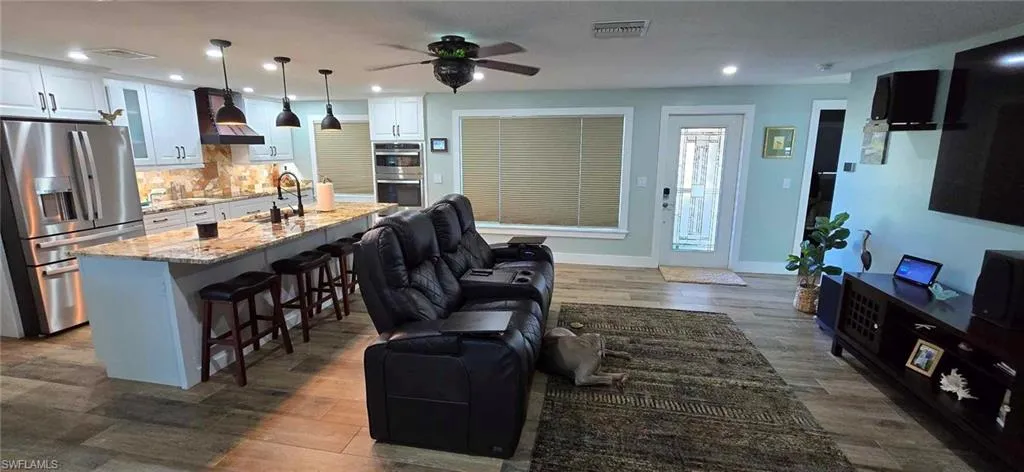 Kitchen featuring white cabinets, open floor plan, appliances with stainless steel finishes, wall chimney range hood, and a kitchen bar