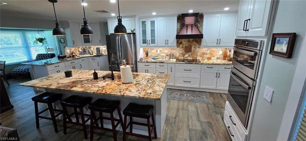 Kitchen featuring a breakfast bar, a center island with sink, custom range hood, glass insert cabinets, and stainless steel fridge with ice dispenser