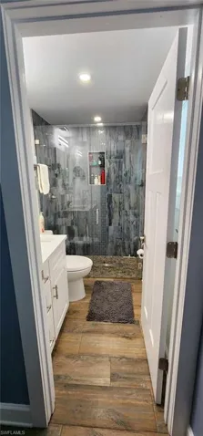 Full bath featuring a stall shower, vanity, toilet, and wood finished floors