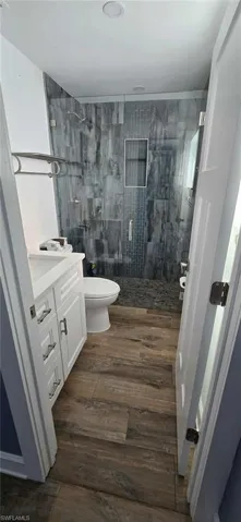 Bathroom with toilet, wood finished floors, vanity, and a stall shower