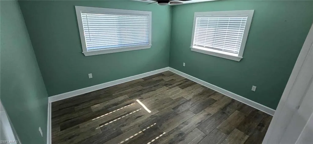 Unfurnished room featuring baseboards, a healthy amount of sunlight, dark wood-style floors, and ceiling fan