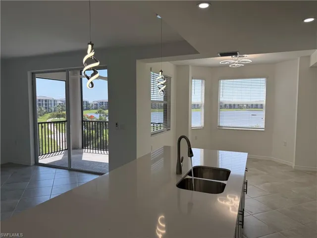 View from modern kitchen island featuring a double stainless steel sink, gooseneck faucet, and light-toned solid surface countertop