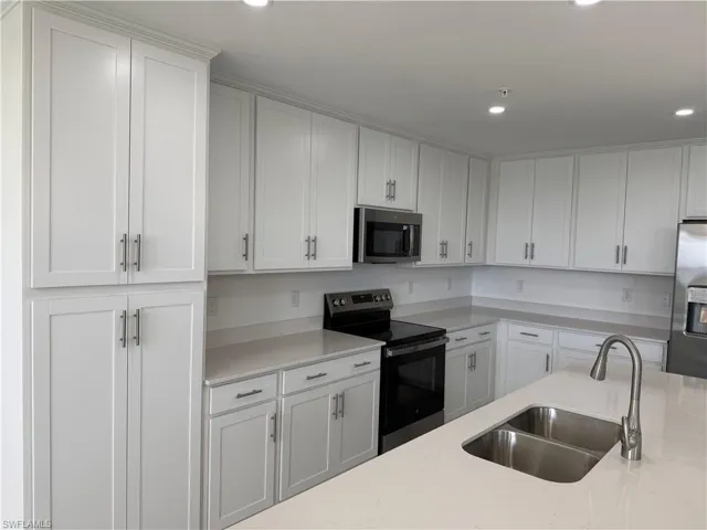 Contemporary kitchen featuring extensive white cabinetry, light countertops, stainless steel appliances, a double basin sink, and recessed lighting