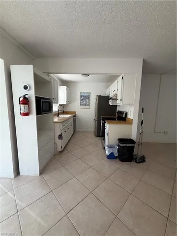 Kitchen featuring white cabinets, a textured ceiling, stove, stainless steel refrigerator, and light countertops