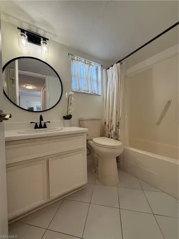 Bathroom featuring vanity, shower / bath combo with shower curtain, a textured ceiling, and light tile patterned floors