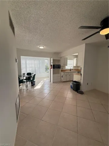 Living area featuring ceiling fan, a textured ceiling, and light tile patterned floors