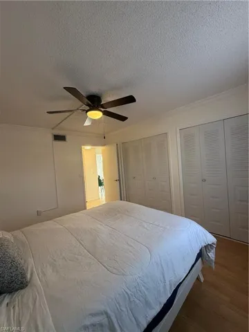 Bedroom with multiple closets, wood finished floors, crown molding, a ceiling fan, and a textured ceiling
