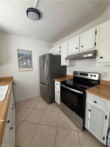 Kitchen featuring range, white cabinetry, range hood, freestanding refrigerator, and a textured ceiling