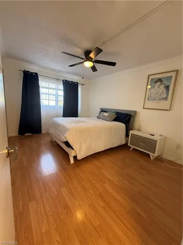 Bedroom featuring ornamental molding, a ceiling fan, light wood-style flooring, and a textured ceiling