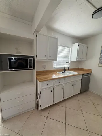 Kitchen with a textured ceiling, white cabinetry, light tile patterned flooring, dishwashing machine, and wooden counters