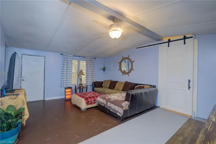 Living room featuring baseboards, vaulted ceiling with beams, a barn door, and a ceiling fan