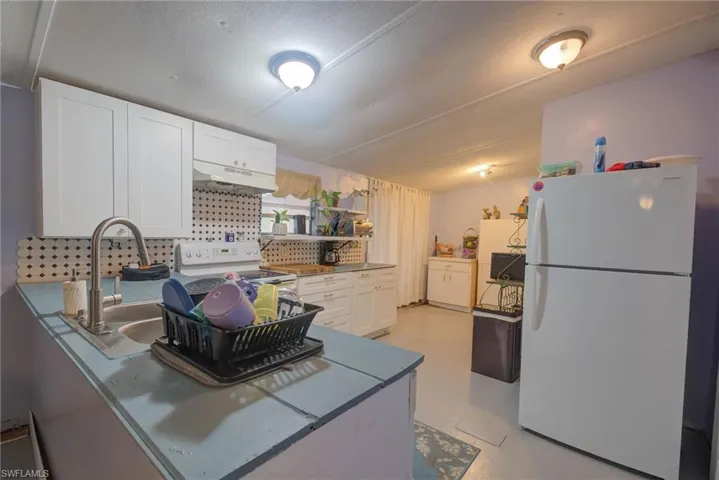 Kitchen with white appliances, a peninsula, white cabinets, under cabinet range hood, and a sink