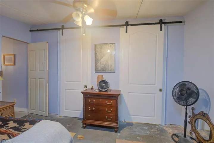 Bedroom with a barn door, concrete flooring, and ceiling fan