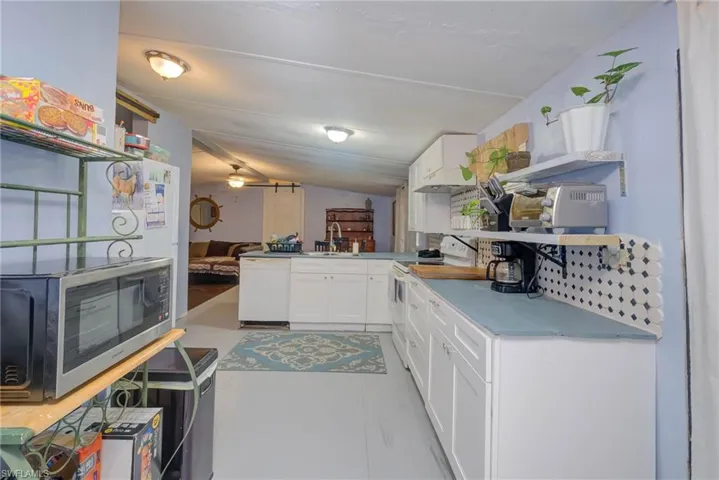 Kitchen with a peninsula, white cabinetry, a sink, and white appliances