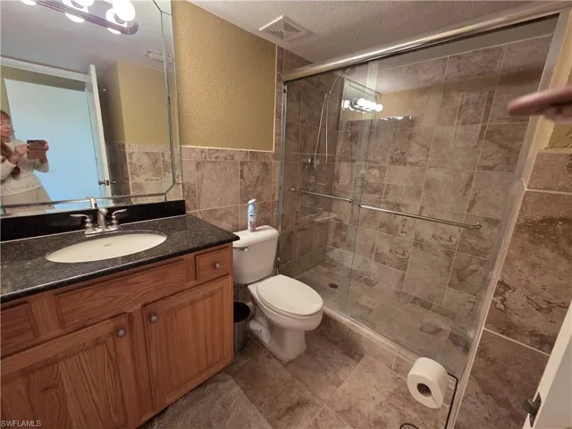 Full bathroom with vanity, tile walls, a textured wall, a shower stall, and a textured ceiling