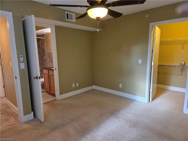 Unfurnished bedroom featuring a spacious closet, light colored carpet, ensuite bath, and ceiling fan