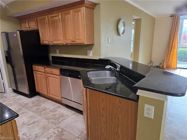 Kitchen featuring wood finish cabinetry, stainless steel appliances, dark stone counters, a peninsula, and crown molding