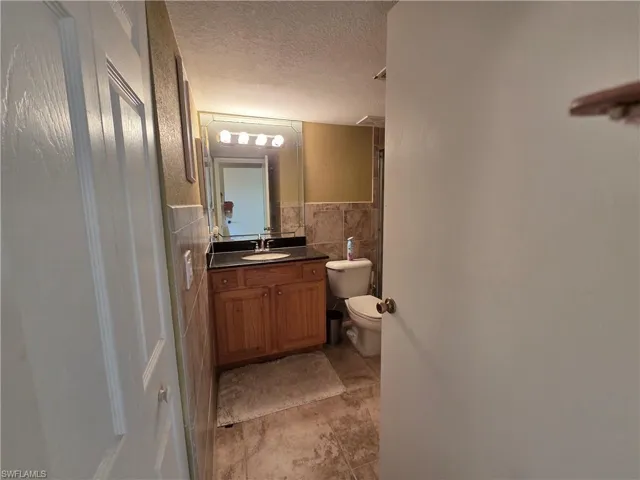 Bathroom featuring a textured ceiling, vanity, tile walls, and wainscoting