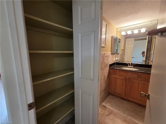 Bathroom with a textured ceiling, vanity, a closet, tile walls, and a wainscoted wall