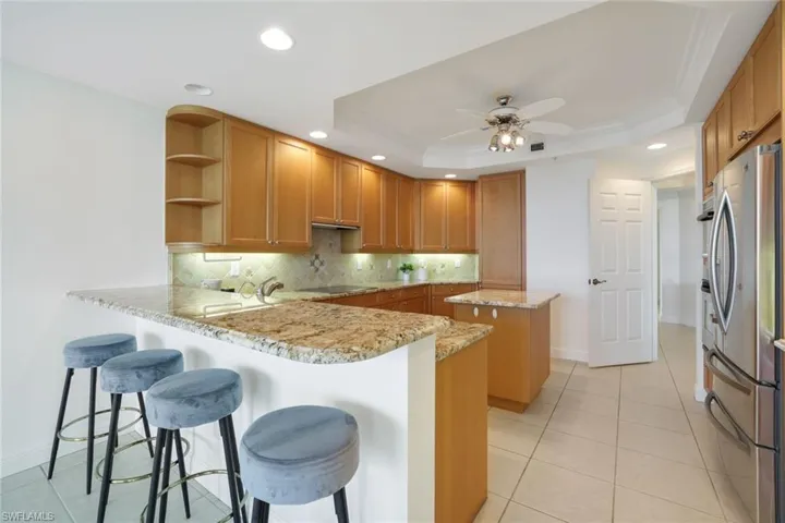 Kitchen featuring a kitchen island, kitchen peninsula, a tray ceiling, a kitchen bar, and stainless steel refrigerator