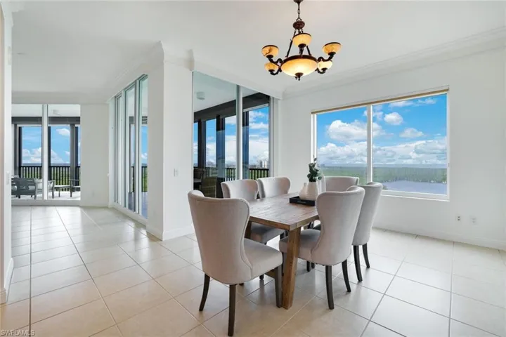 Dining space with ornamental molding, a chandelier, light tile patterned flooring, and a water view