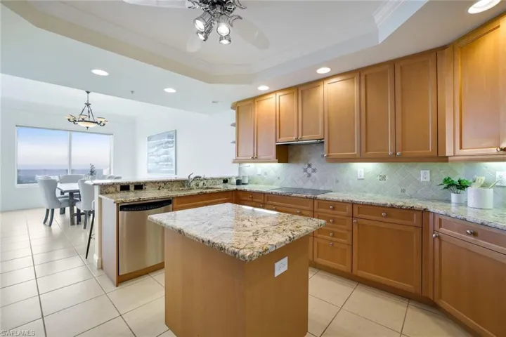Kitchen featuring ornamental molding, stainless steel dishwasher, a raised ceiling, and a kitchen island