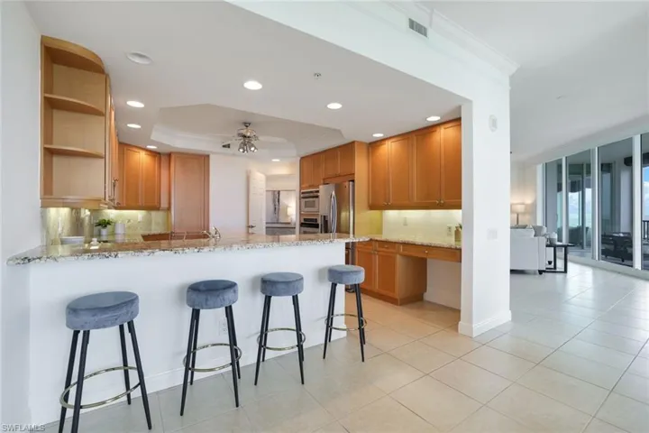 Kitchen with kitchen peninsula, ceiling fan, appliances with stainless steel finishes, light stone countertops, and a tray ceiling