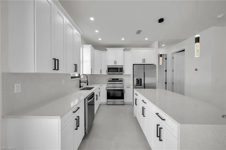 Kitchen featuring sink, decorative light fixtures, a center island, appliances with stainless steel finishes, and white cabinets