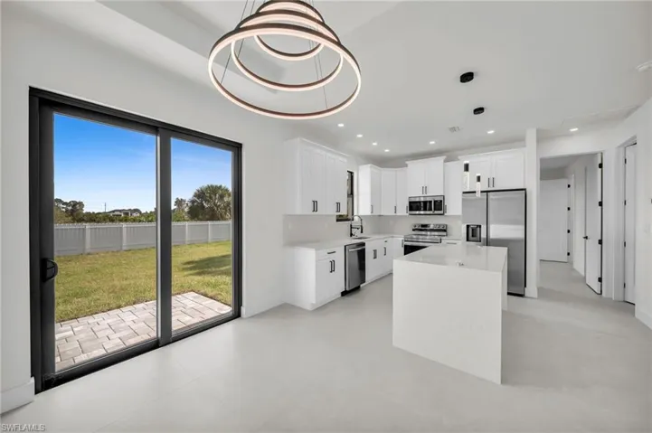 Kitchen featuring sink, white cabinetry, stainless steel appliances, a center island, and decorative light fixtures
