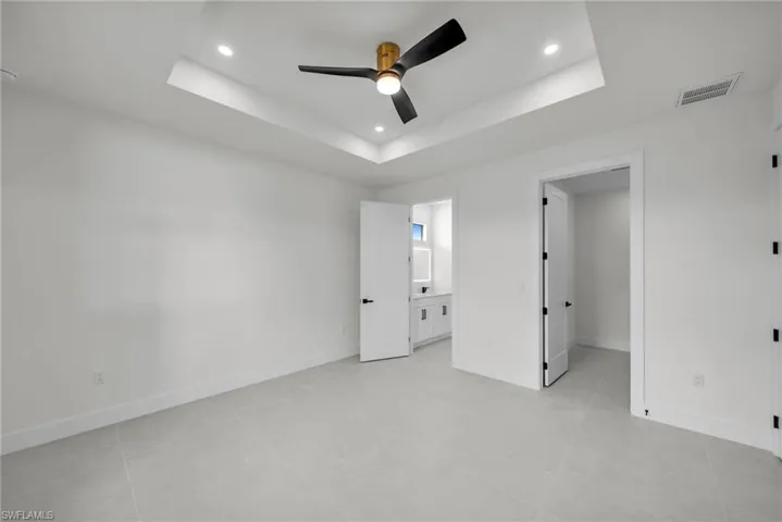 Unfurnished bedroom with a tray ceiling, ensuite bath, ceiling fan, and light tile patterned flooring