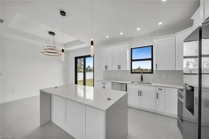 Kitchen with sink, appliances with stainless steel finishes, white cabinets, pendant lighting, and backsplash